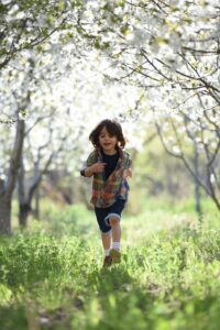 Boy running through field lined by trees