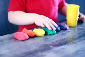 Closeup of young child in a red shirt playing with rainbow Playdoh
